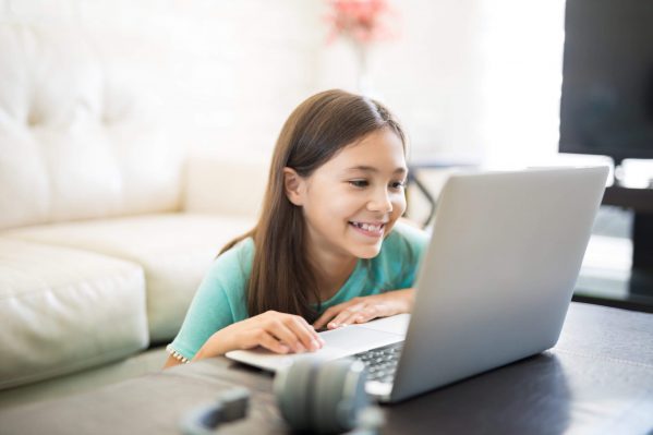 A girl smiling while playing on their laptop.