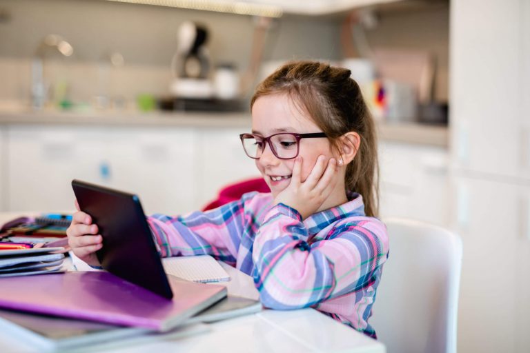 An image of a girl smiling while holding her tablet.