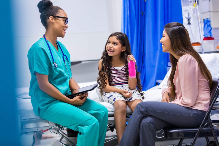 A nurse seated with a patient in a cast and her mother in a hospital room.