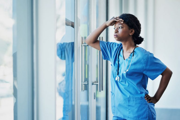 An overwhelmed nurse looking outside of a window.