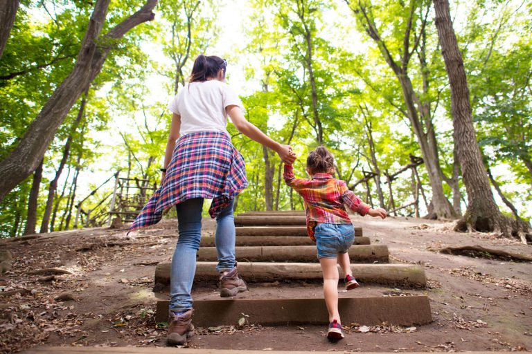 A mother and a daughter climbing a small flight of stairs in an outdoor trail.