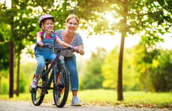 A mother helping her daughter ride her bicycle.