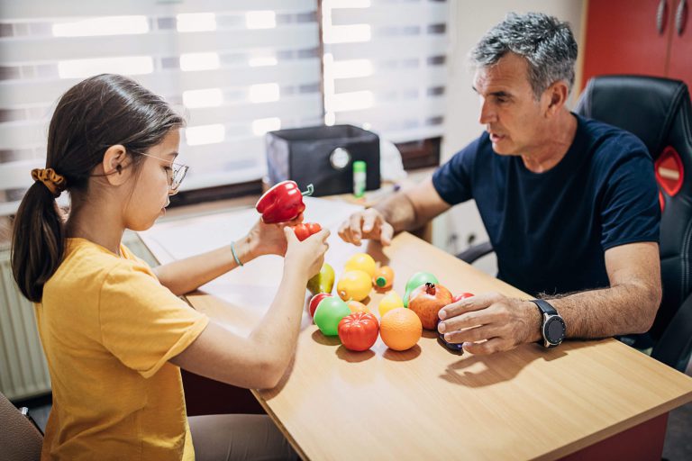 A professional and a student inspecting a group of sensory shaped fruits.