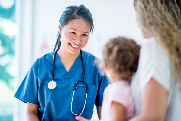 A nurse smiling at a small girl and her mother.