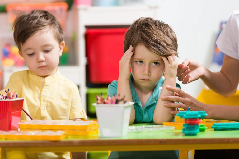 A frustrated young boy with a teacher attempting to console them.