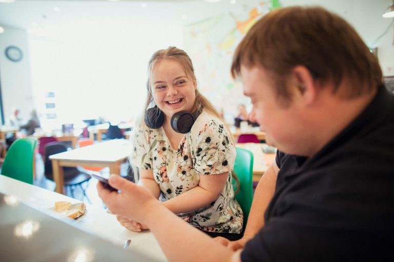 Two friends seated in a classroom talking about music.