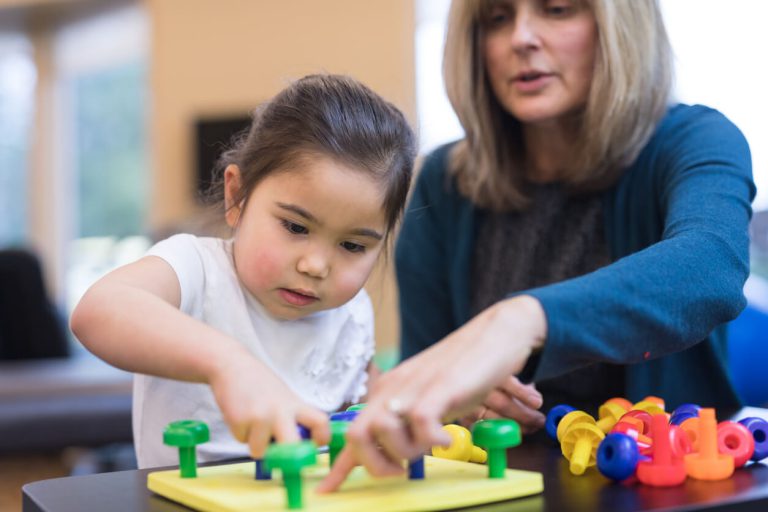 A teacher and a student placing different color pegs into a base.