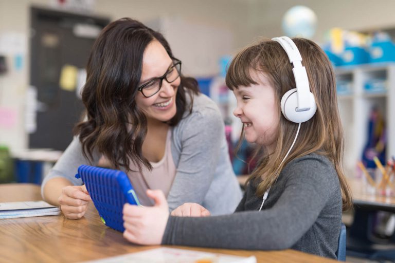 iStock-956516080-1680 A smiling girl with headphones and a tablet next to an educational diagnostician.