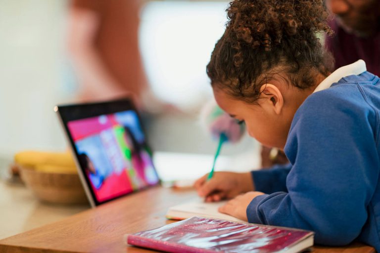 A student taking notes from what they are shown on a laptop.
