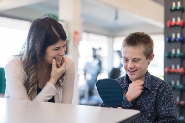 A speech language pathologist and her student practicing mouth movements in front of a mirror.