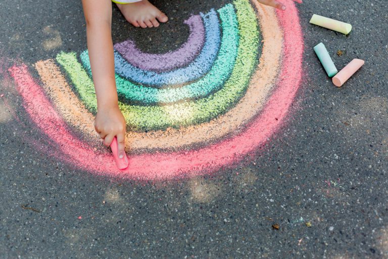 A child drawing a chalk rainbow on the pavement.